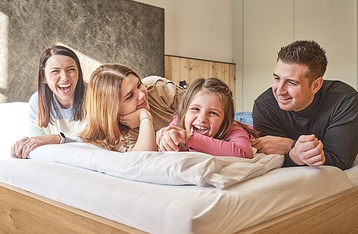 Fröhliche Familie mit zwei Kindern lacht und tobt gemeinsam auf dem Bett im Hotelzimmer