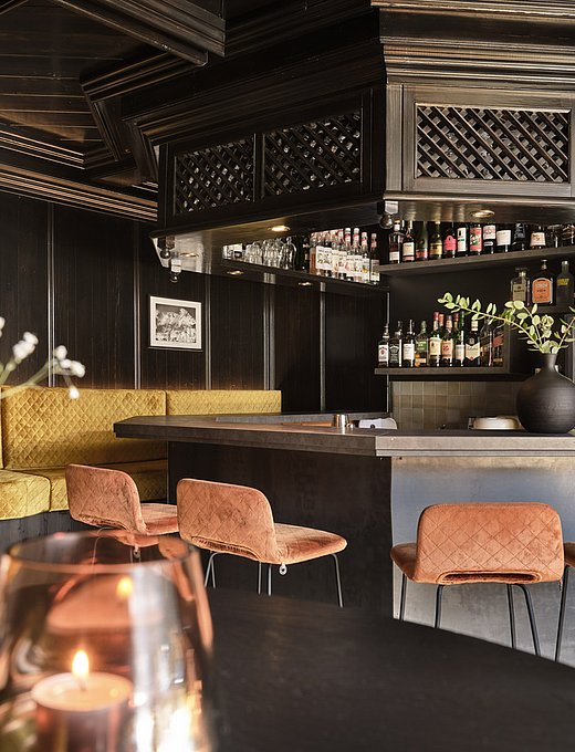 Elegante Hotelbar mit dunklem Holz, goldener Sitzbank, Flaschenregal und gemütlichem Ambiente