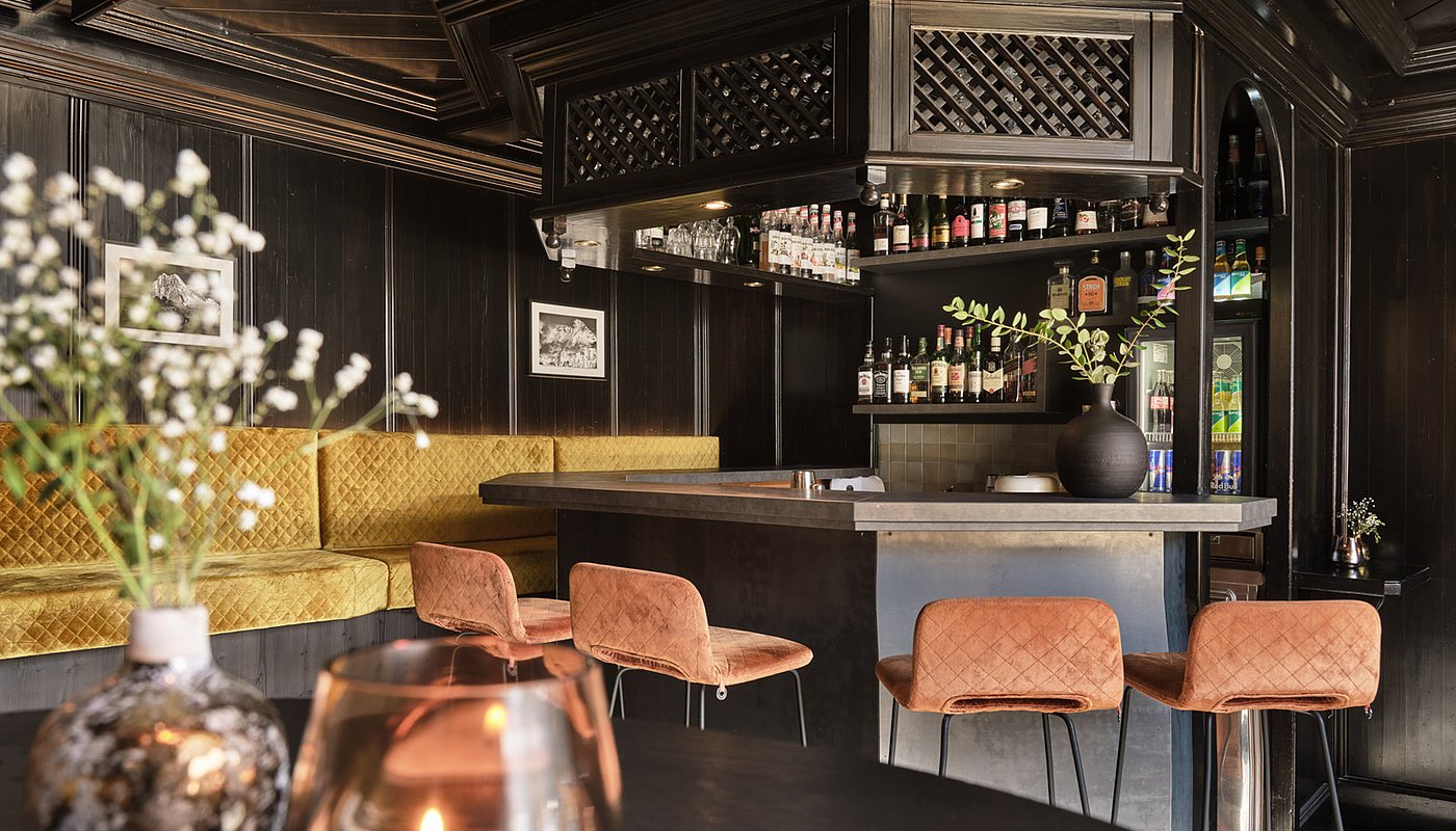 Elegante Hotelbar mit dunklem Holz, goldener Sitzbank, Flaschenregal und gemütlichem Ambiente