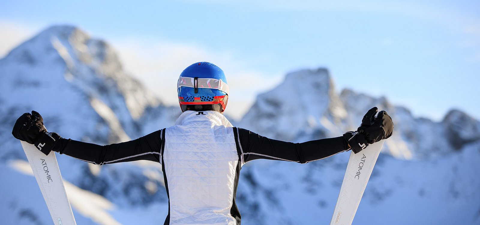 Skifahrerin mit ausgestreckten Armen blickt auf verschneite Berggipfel im Winter