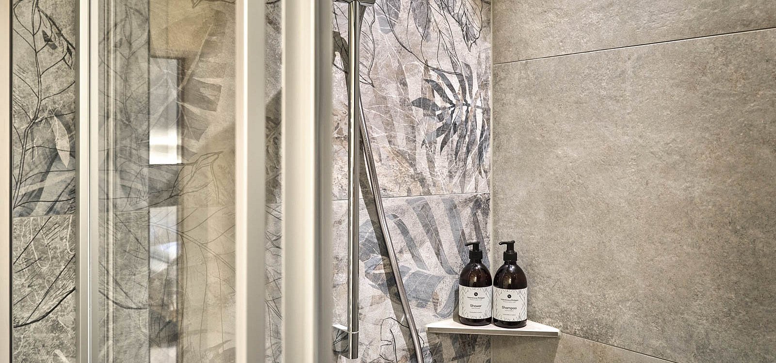 Dusche mit floraler Natursteinoptik und Pflegeprodukten auf Glasablage