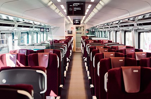 Moderner ÖBB-Zuginnenraum mit roten Sitzen und Gangansicht