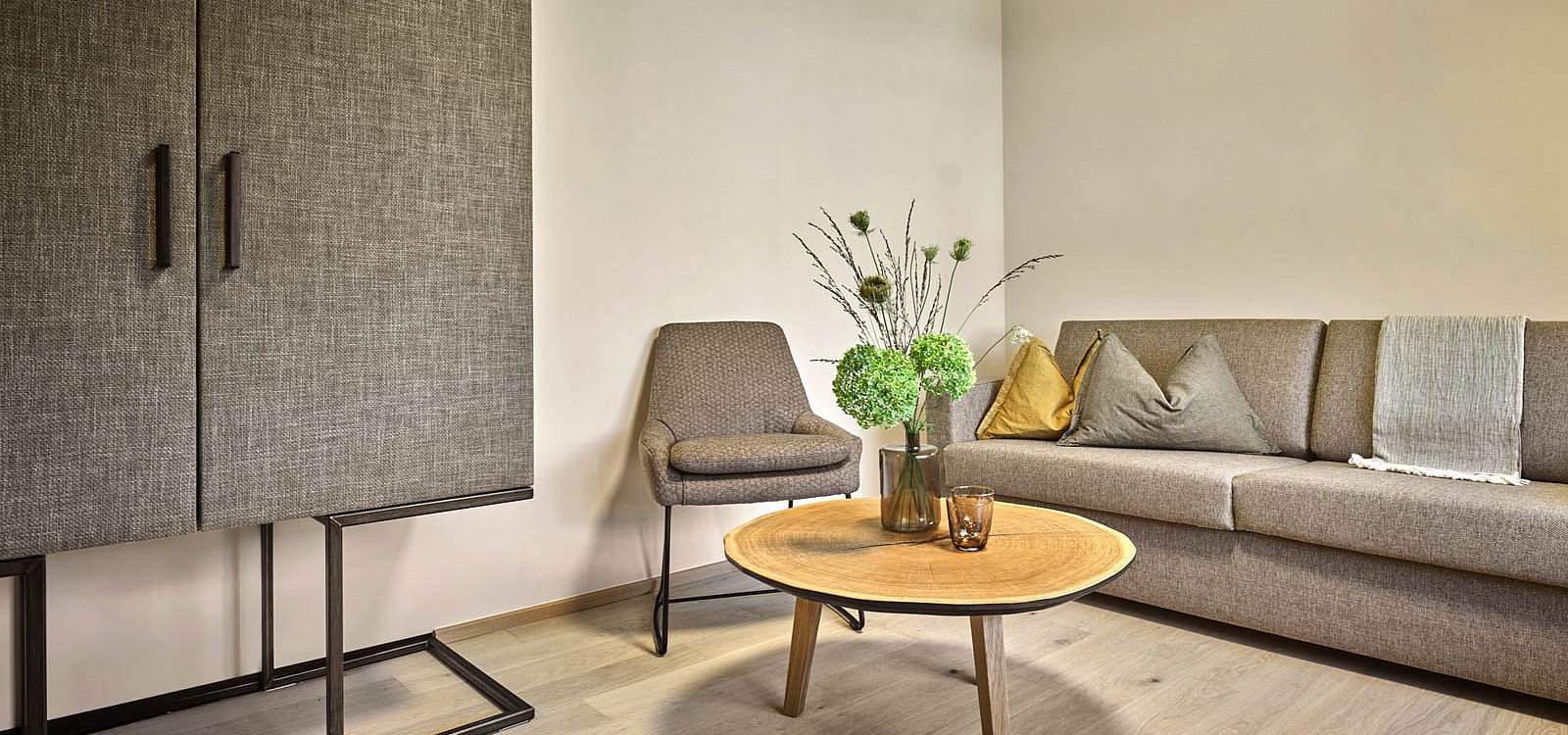 Heller Wohnbereich mit Sofa, grauem Sessel und Holztisch mit grüner Blumendeko