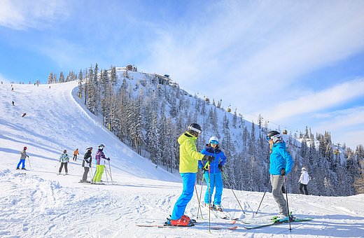 Skifahrergruppe genießt sonnigen Skitag auf breiter, schneebedeckter Abfahrt mit Wald