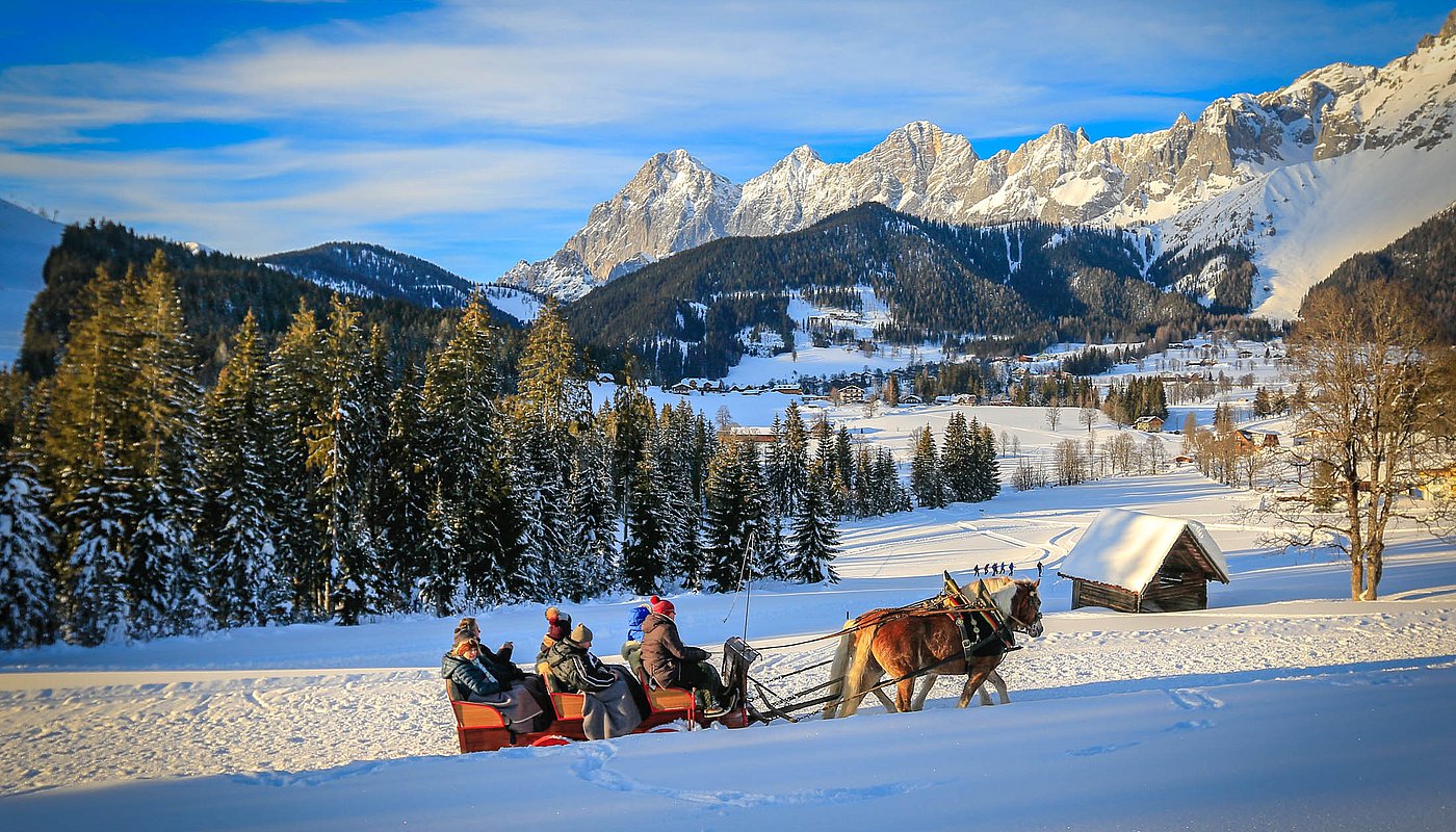 Pferdeschlittenfahrt durch verschneite Landschaft mit Blick auf Bergdorf