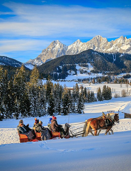 Pferdeschlittenfahrt durch verschneite Landschaft mit Blick auf Bergdorf