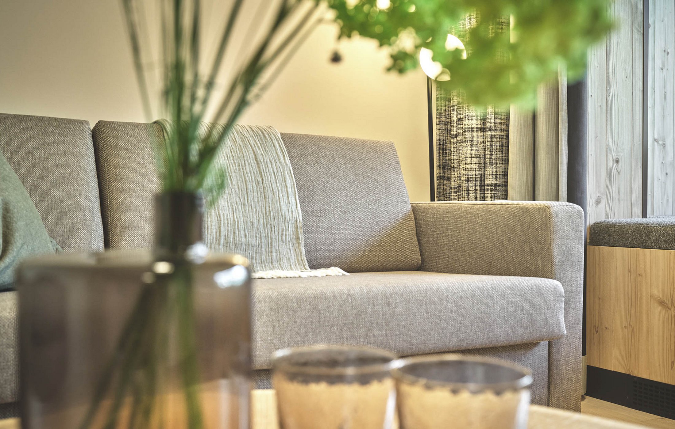 Close-up of couch with cushions, flower vase on table in the foreground
