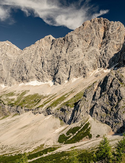 Massives Felsmassiv mit Geröllfeldern, Wiesenflächen und vereinzelten Schneeresten