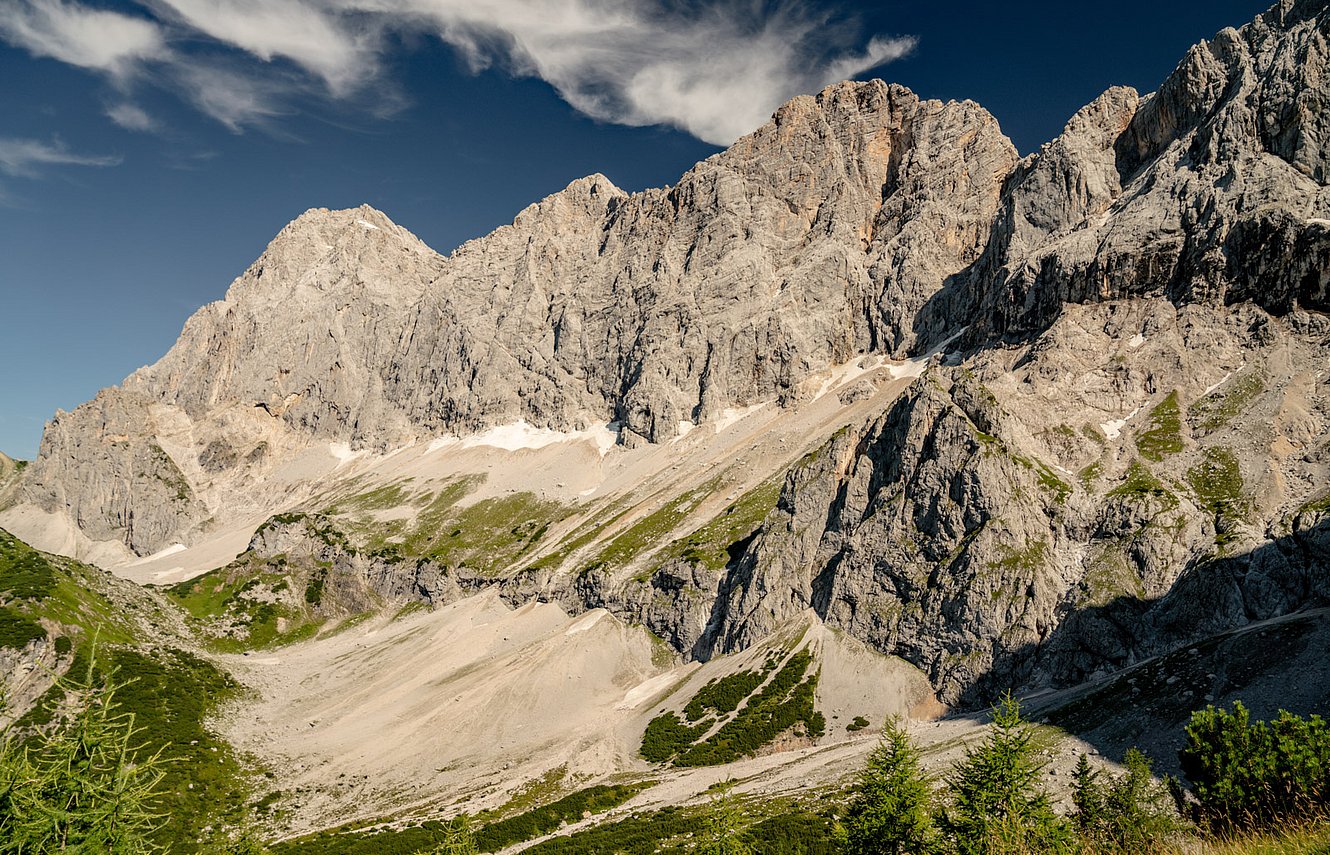 Massives Felsmassiv mit Geröllfeldern, Wiesenflächen und vereinzelten Schneeresten