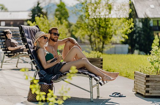 Paar sonnt sich auf Liegestühlen im Gartenbereich der Therme bei sommerlichem Wetter