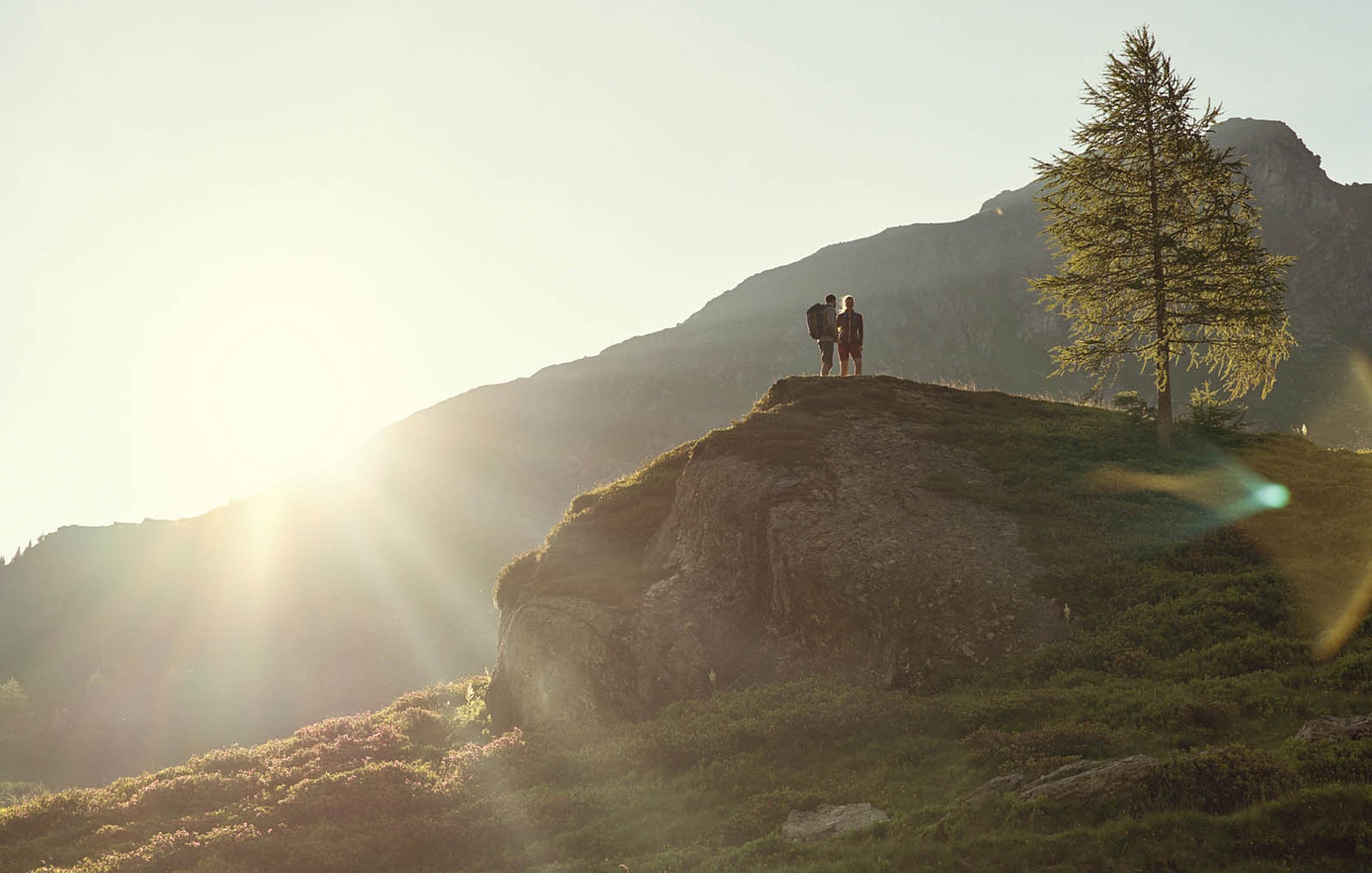 Paar auf Felsplateau in Abendstimmung mit Blick ins Tal und Bergsilhouette