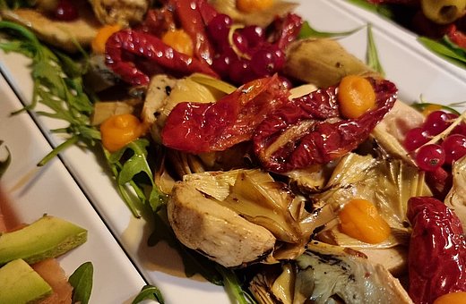 Antipasti mit Artischocken, getrockneten Tomaten, Beeren und Rucola, kunstvoll angerichtet