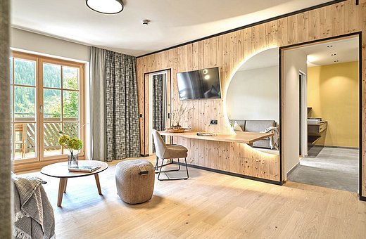 Wohnbereich mit Balkonzugang, Couch, Schreibtisch und Naturblick