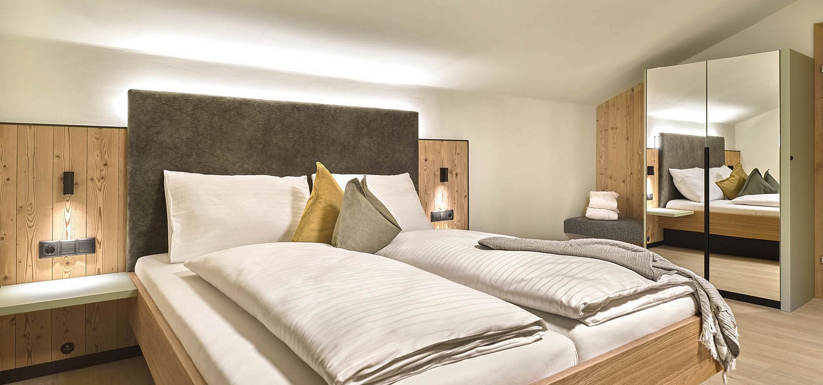 Modernes Hotelzimmer mit Doppelbett, Spiegel und Holzelementen unter schräger Decke