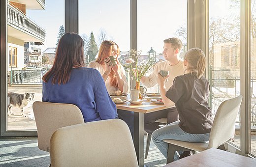 Group of four people drinking coffee at a table in the sun-filled hotel restaurant with a view of the winter garden