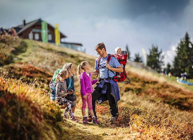 Familie beim Wandern auf buntem Herbstweg mit Baby in Rückentrage und Bergkulisse