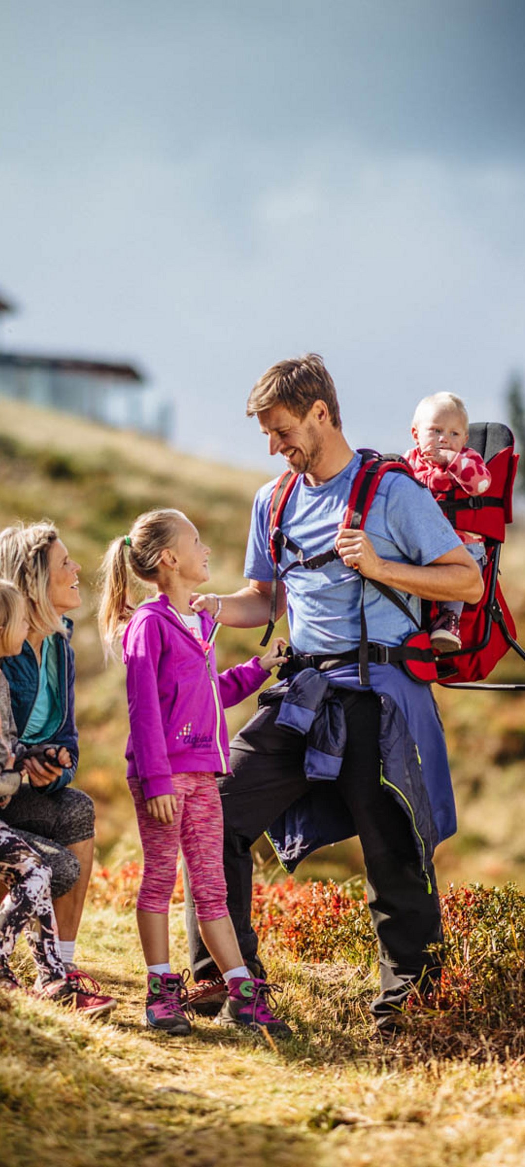 Familie beim Wandern auf buntem Herbstweg mit Baby in Rückentrage und Bergkulisse