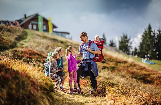 Familie beim Wandern auf buntem Herbstweg mit Baby in Rückentrage und Bergkulisse