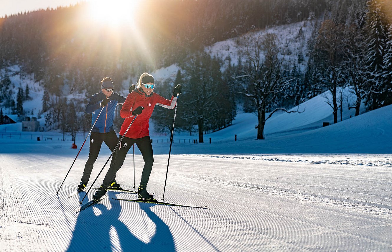 Zwei Langläufer bei Sonnenuntergang auf perfekt gespurter Loipe im Tal