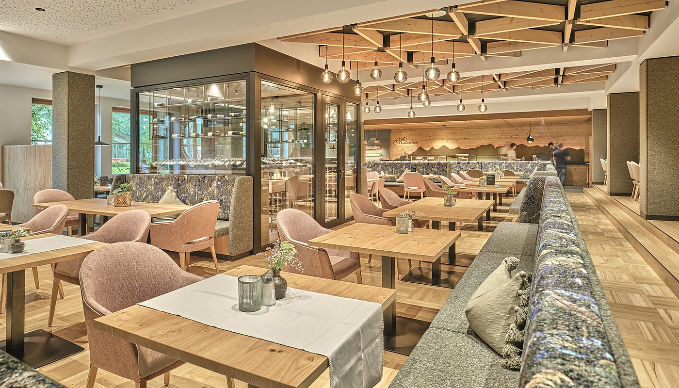 Moderner, heller Restaurantbereich mit Holztischen, Polstermöbeln und stylischer Decke