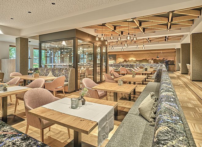 Moderner, heller Restaurantbereich mit Holztischen, Polstermöbeln und stylischer Decke