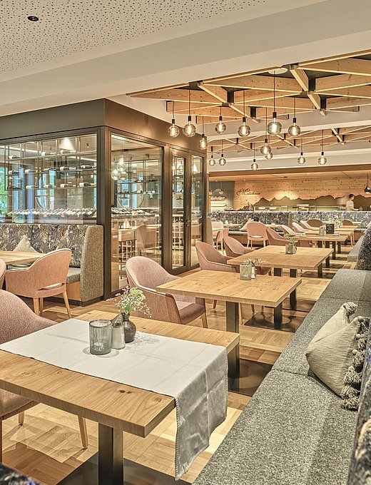 Moderner, heller Restaurantbereich mit Holztischen, Polstermöbeln und stylischer Decke