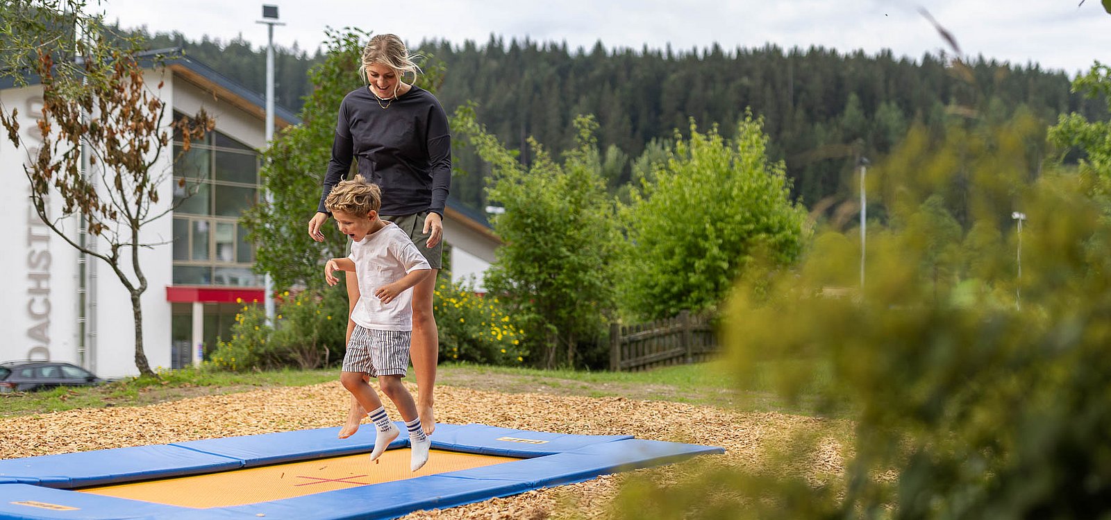 Eine Frau und ein kleiner Junge hüpfen gemeinsam auf einem im Boden eingelassenen Trampolin