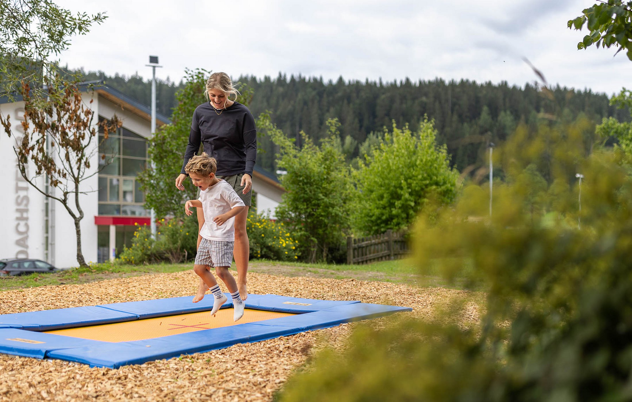 Eine Frau und ein kleiner Junge hüpfen gemeinsam auf einem im Boden eingelassenen Trampolin