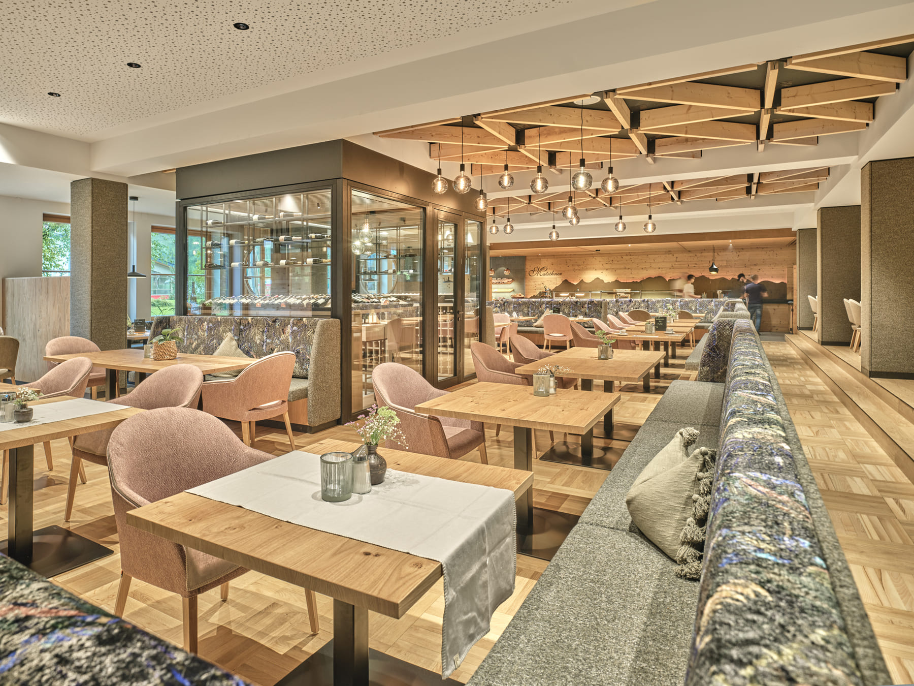Moderner, heller Restaurantbereich mit Holztischen, Polstermöbeln und stylischer Decke