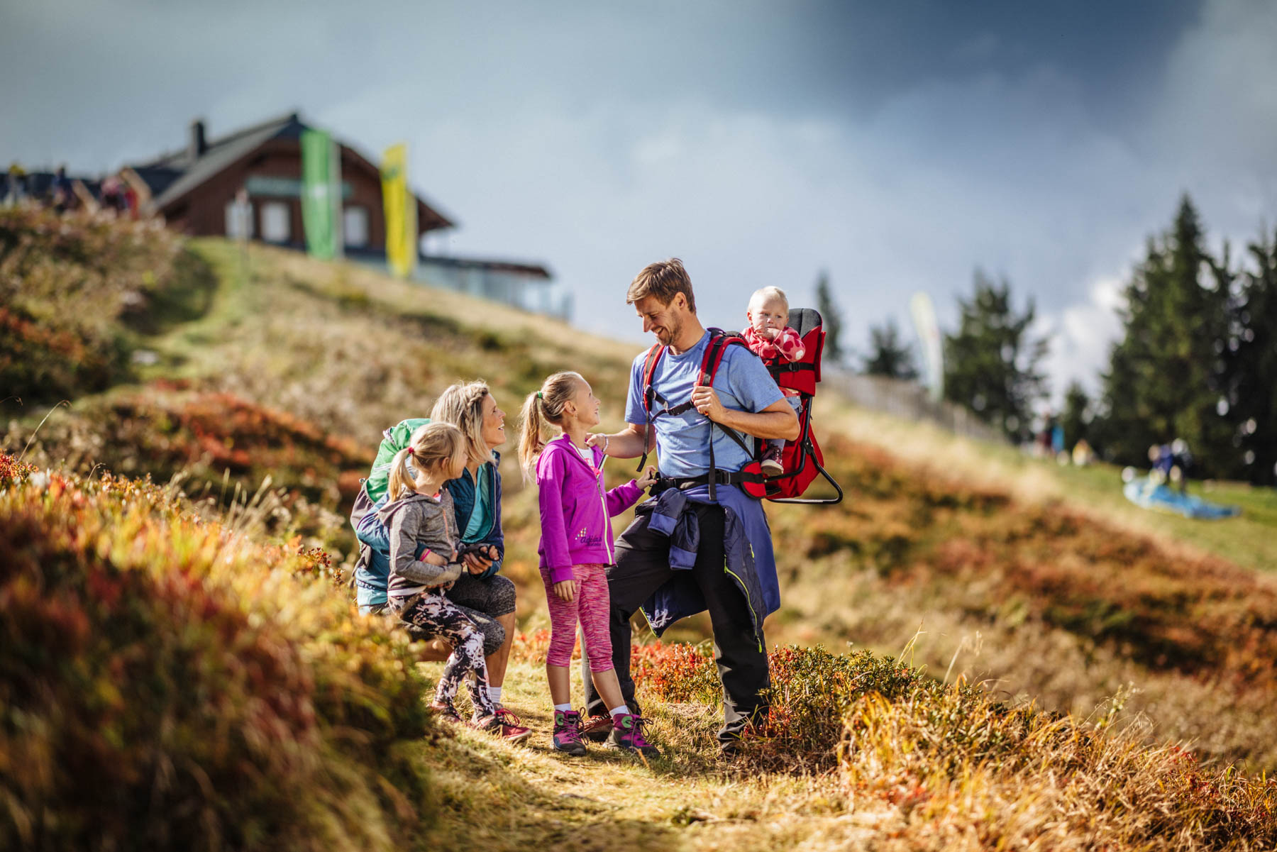 Familie beim Wandern auf buntem Herbstweg mit Baby in Rückentrage und Bergkulisse